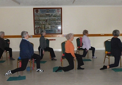 A chair and standing class in a hall, adults working beside chairs